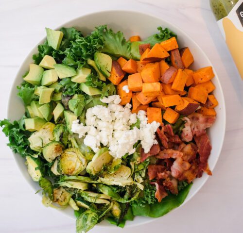 salad topped with sweet potato, brussels sprouts, bacon, goat cheese, gotham greens lemon basil dressing and avocado