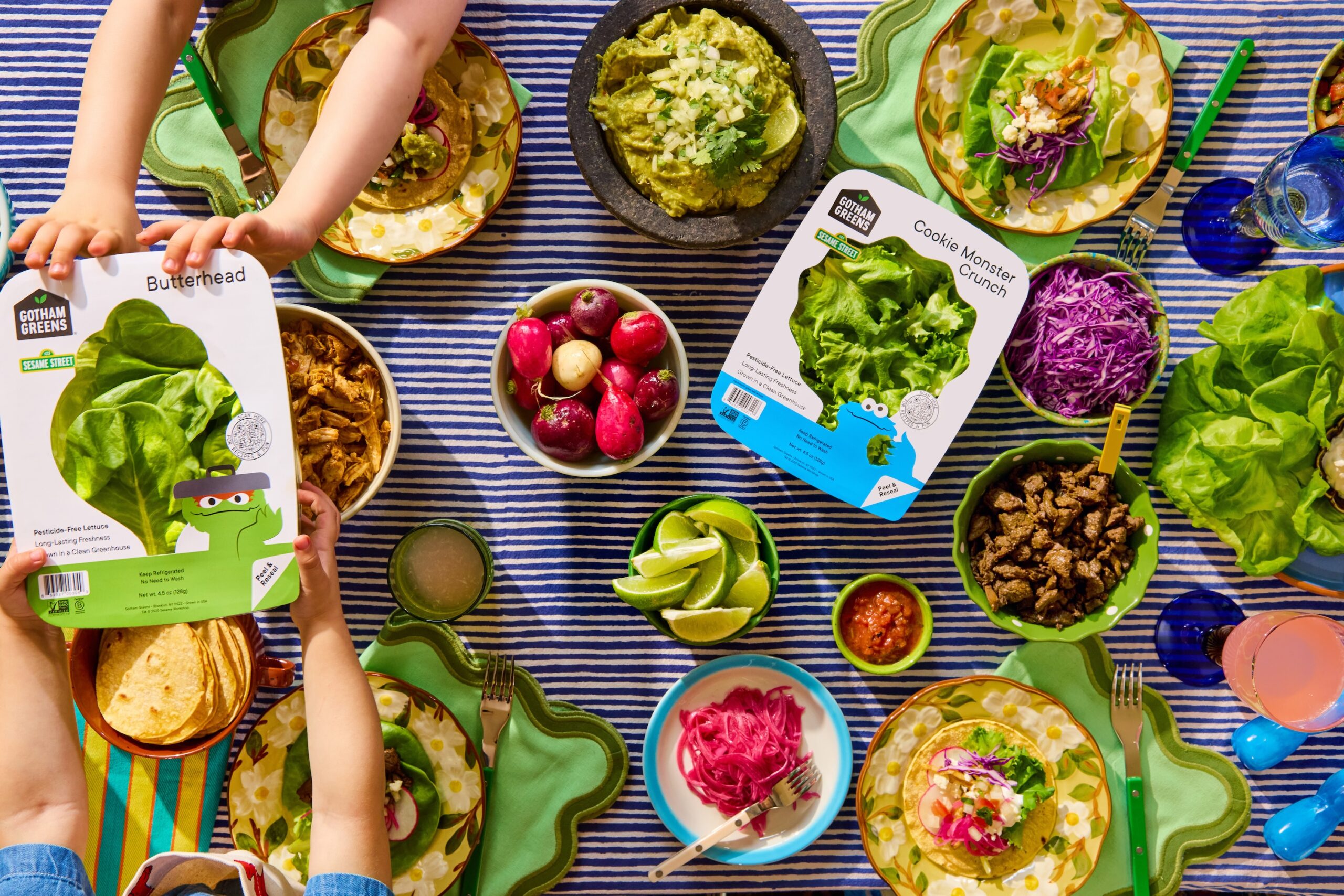 Gotham Greens + Sesame Street collaboration: toddler hands pass a package of lettuce across the table